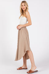 woman wearing a cream strapless top and a beige midi skirt with a high-low hem and button details