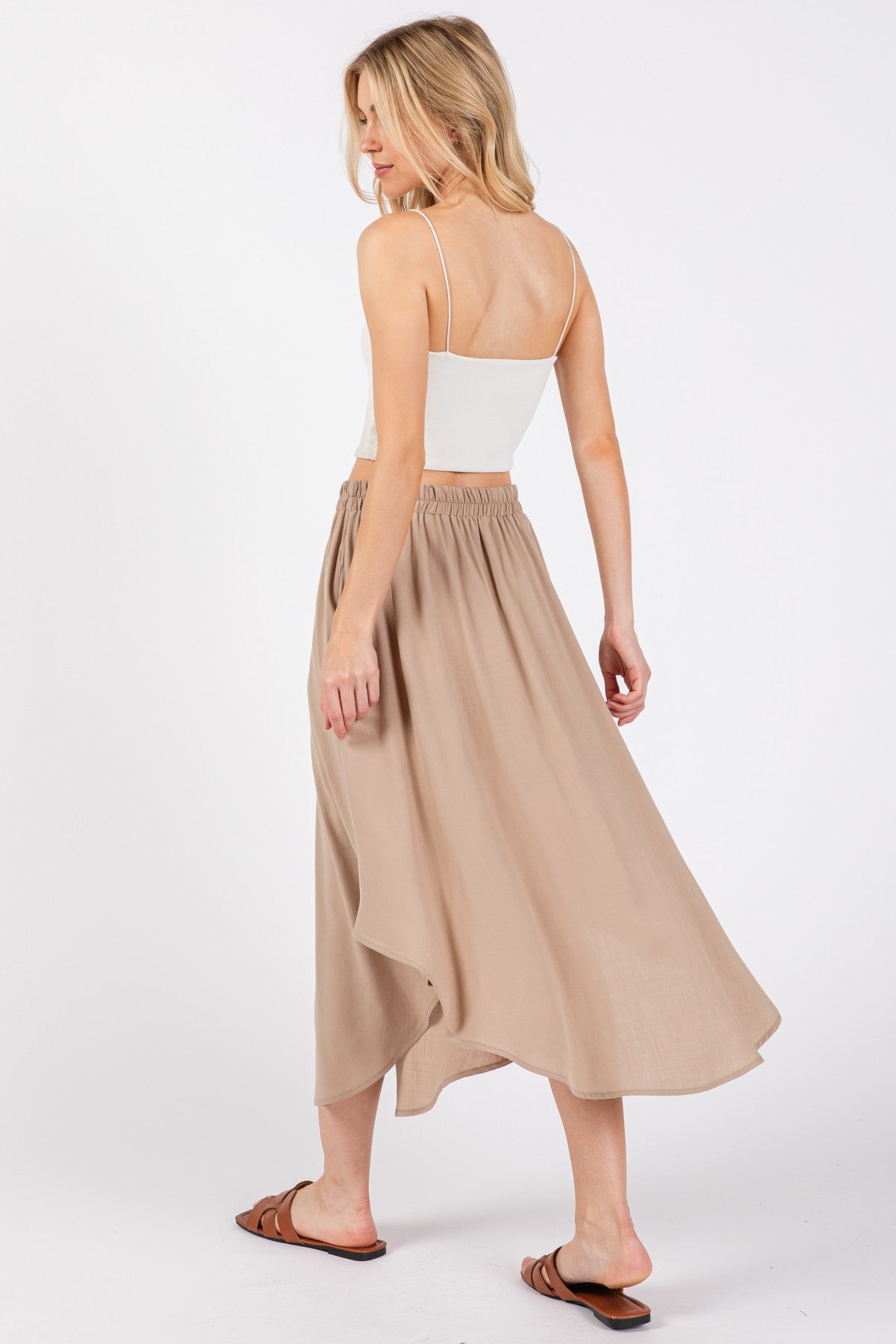woman wearing a white spaghetti strap top and a beige flowy maxi skirt, standing with her back to the camera