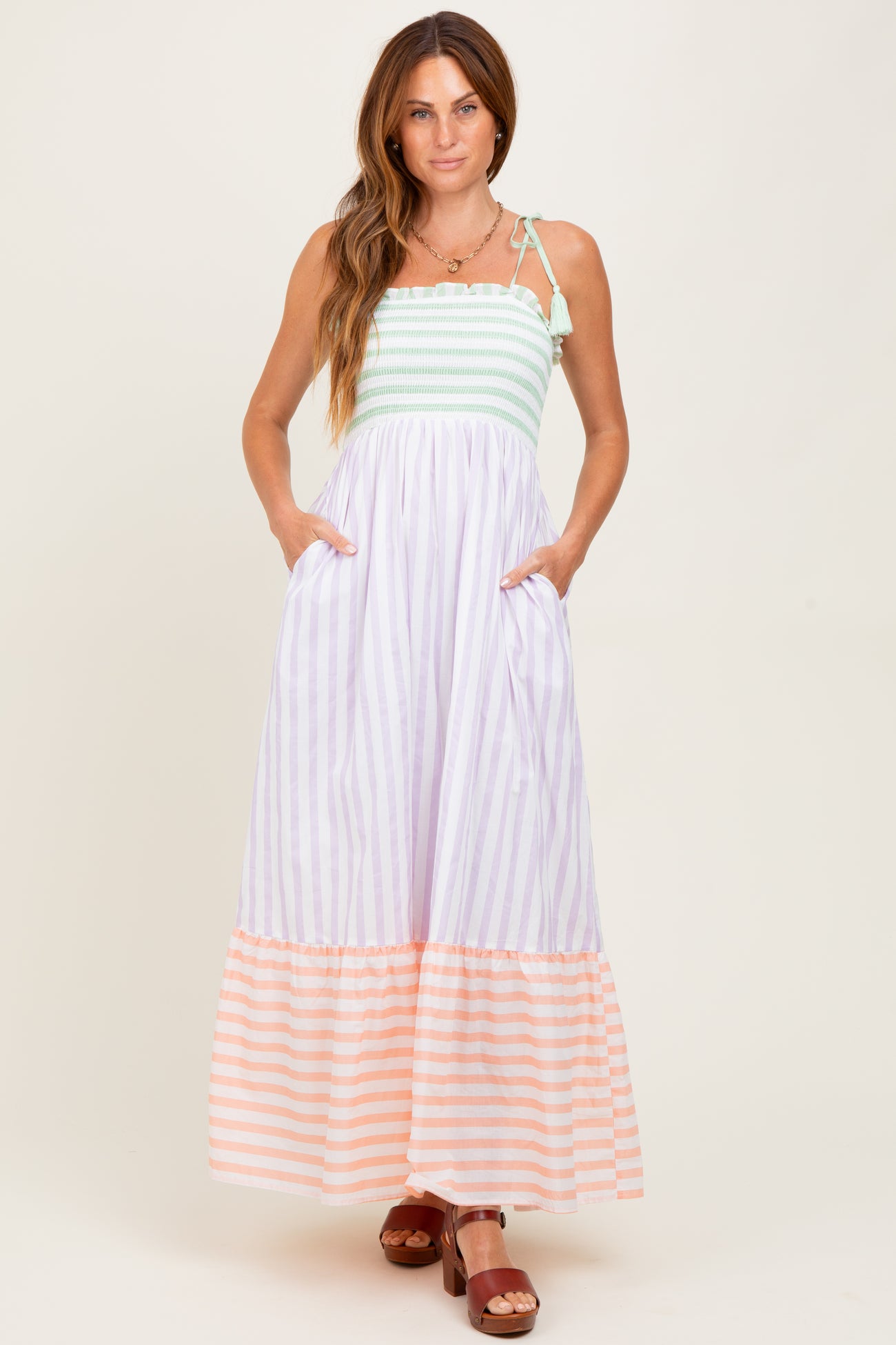 woman wearing a striped maxi dress with a mint top and peach bottom, featuring pockets and adjustable straps