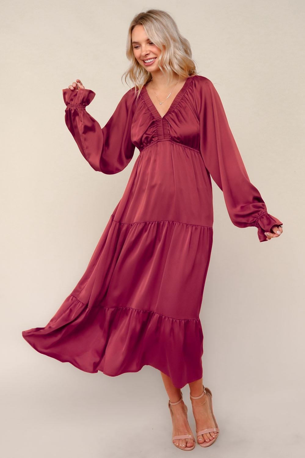 woman wearing a burgundy long sleeve maxi dress with a tiered skirt and puffed sleeves, smiling and in motion