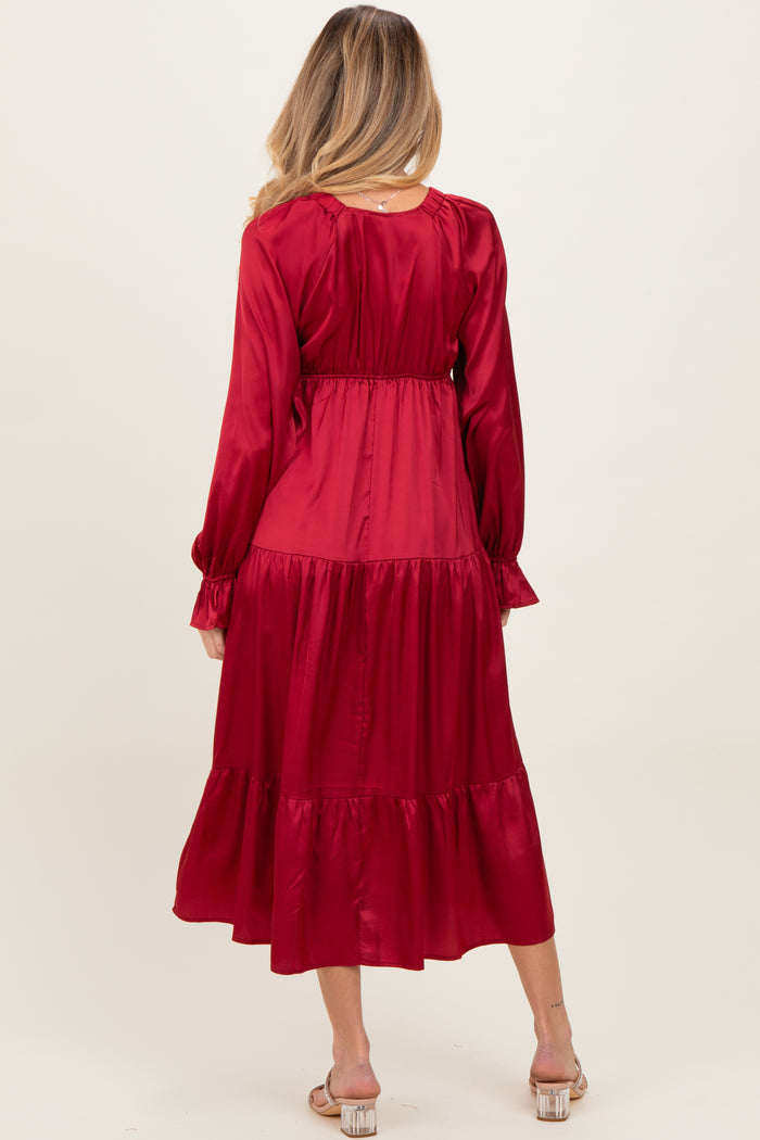 woman wearing a long red satin maternity dress with a tiered skirt and long sleeves, showing a baby bump from the back