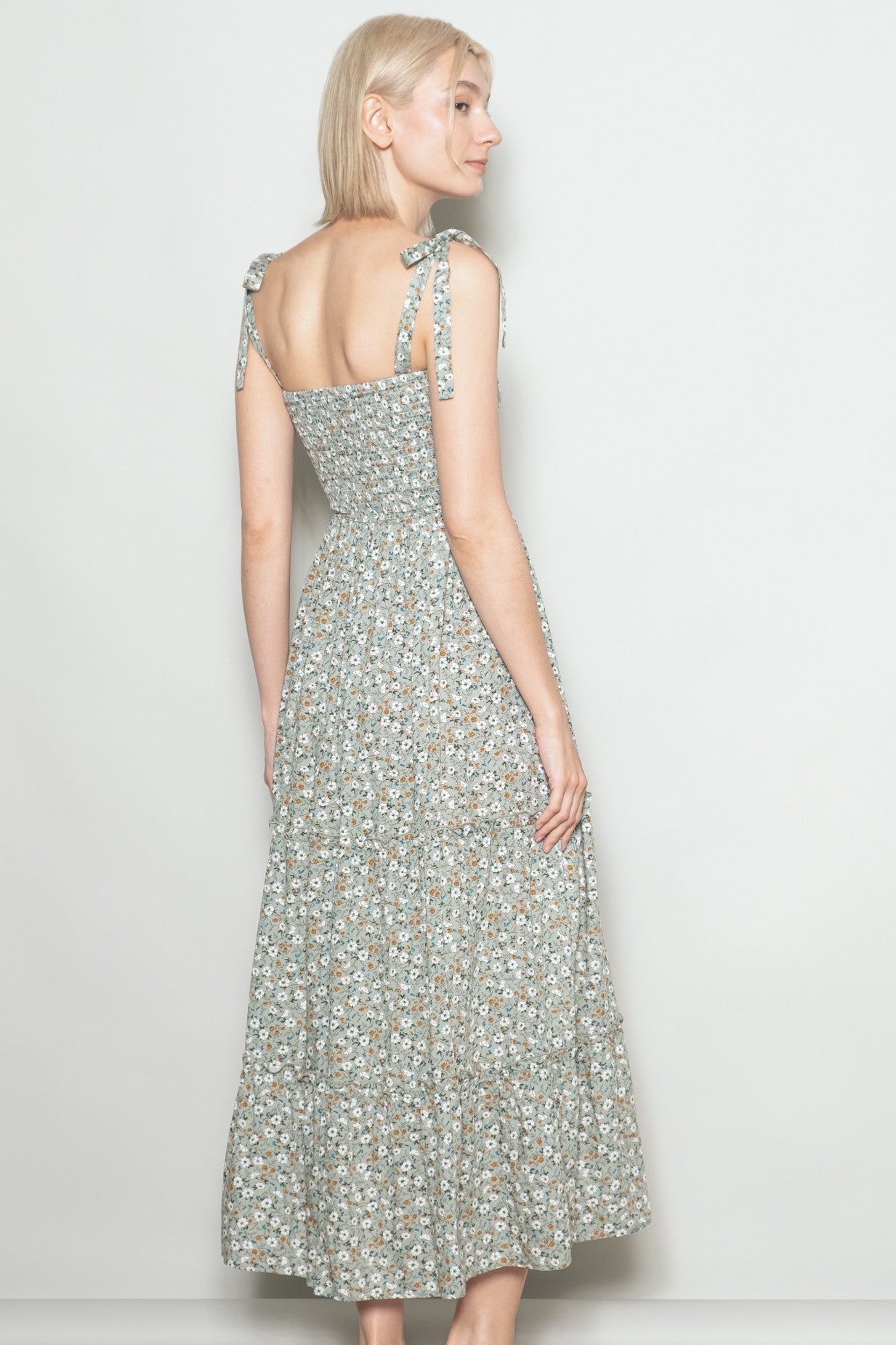 woman wearing a floral print maxi dress with tie straps, showing the back view and a fitted bodice