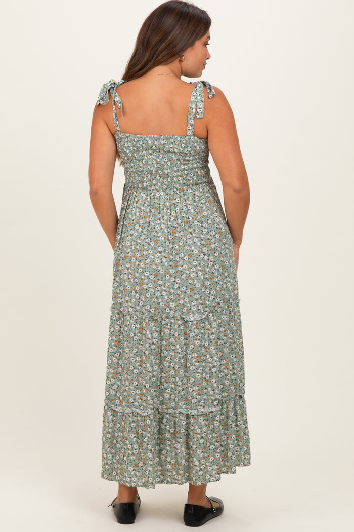 woman wearing a green floral maternity maxi dress with adjustable tie straps and a tiered design
