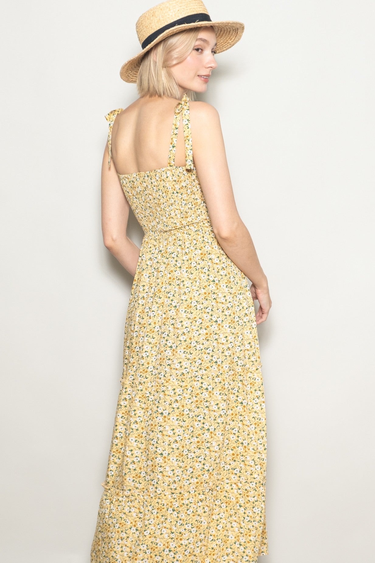 woman wearing a yellow floral maxi dress with shoulder ties and straw hat, turned to show the back view