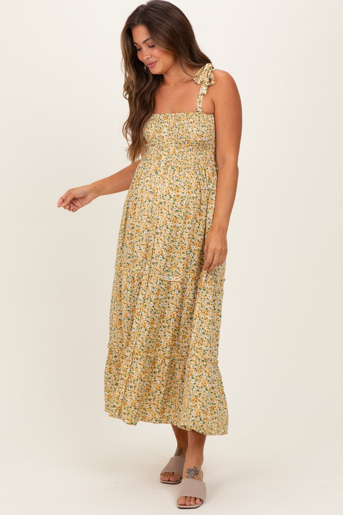 woman wearing a yellow floral maternity maxi dress with a smocked bodice and adjustable straps, showing her baby bump
