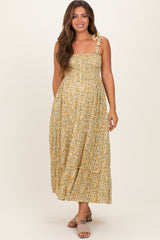 woman wearing a yellow floral maternity dress with adjustable straps and a flowing skirt, styled for a summer look