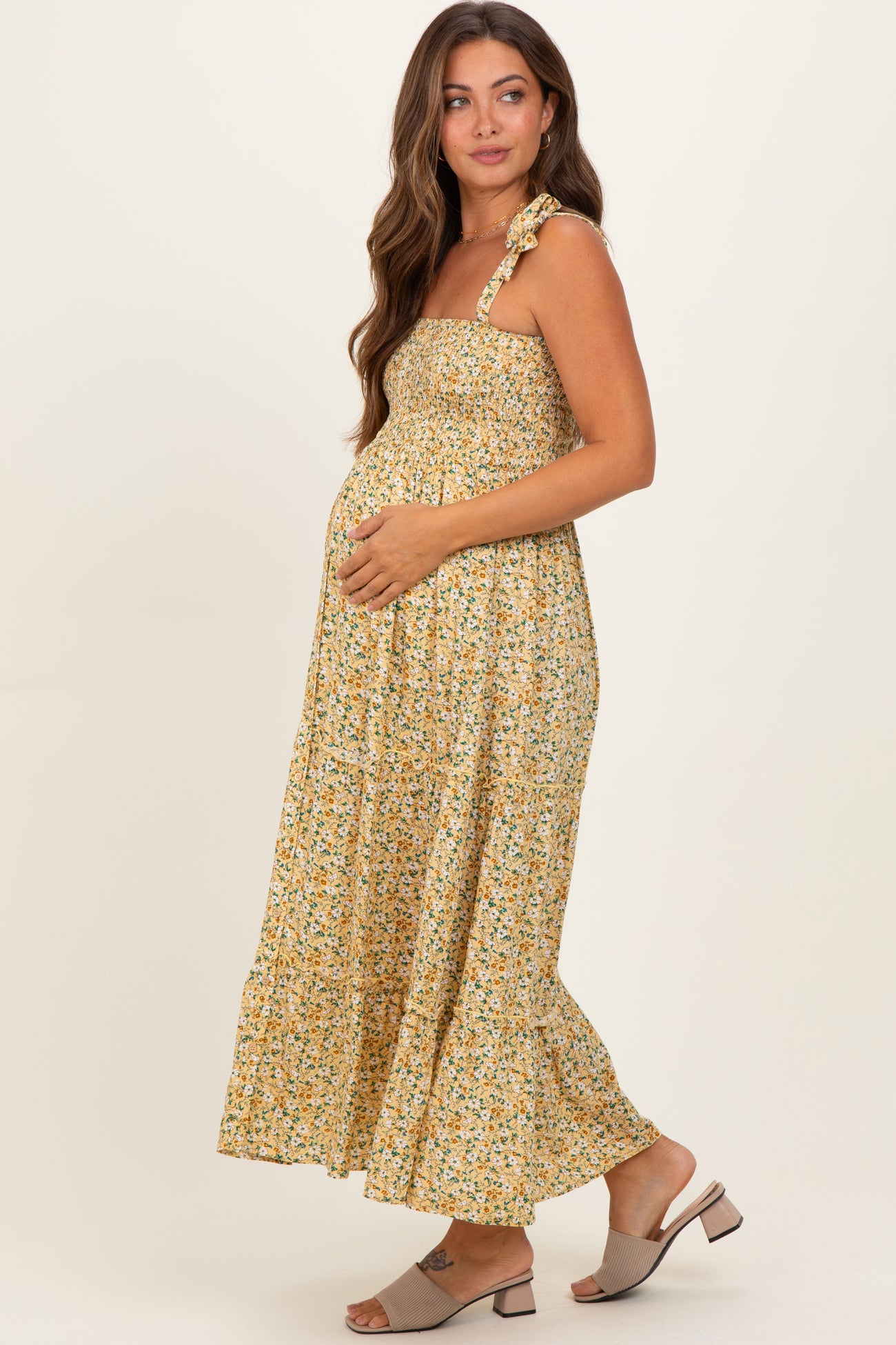 woman wearing a yellow floral maternity dress with a smocked bodice and ruffled hem, holding her baby bump