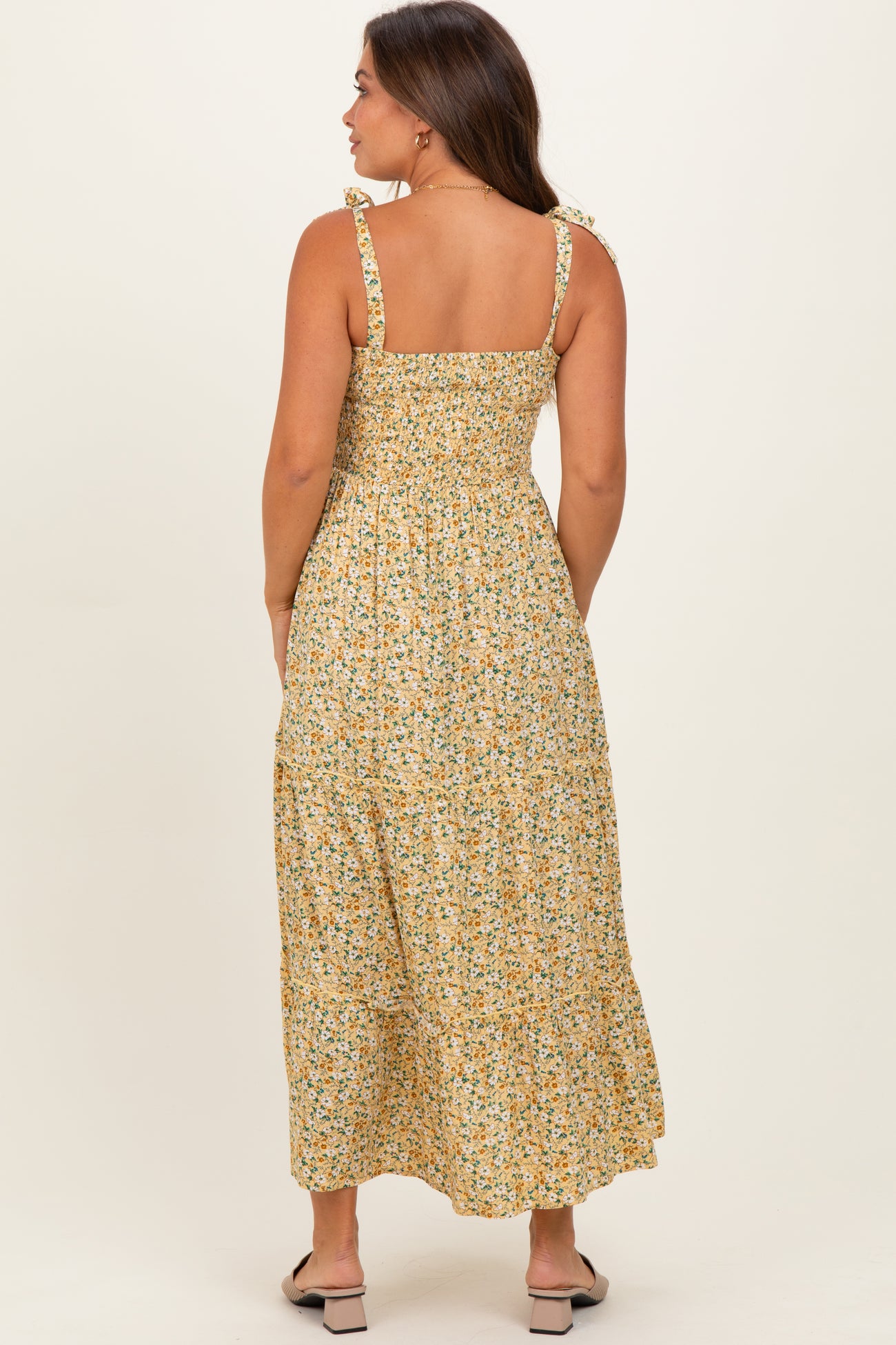 woman wearing a yellow floral maternity maxi dress with adjustable tie straps and a smocked back