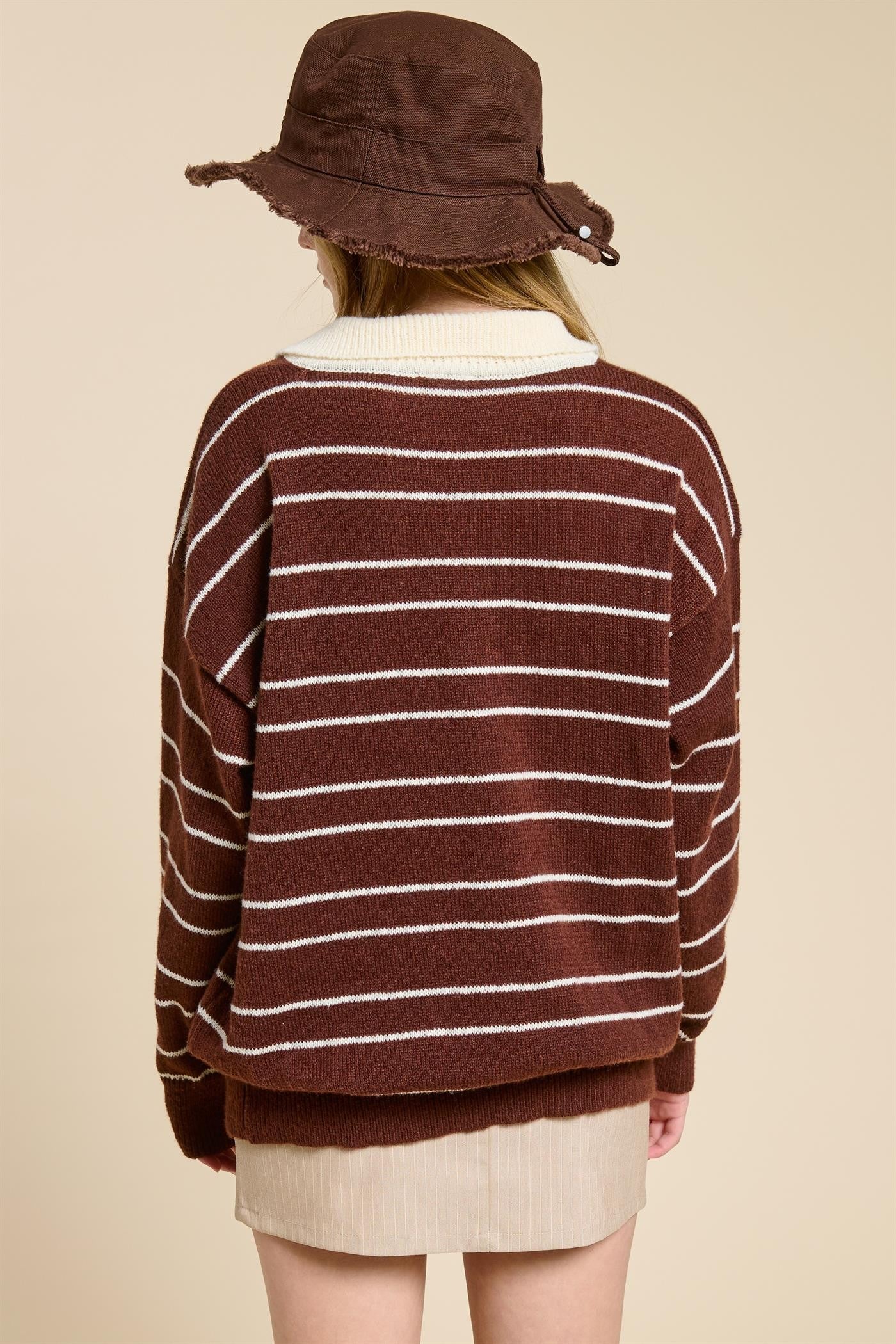 woman wearing a brown and white striped oversized sweater with a wide neckline and a brown bucket hat