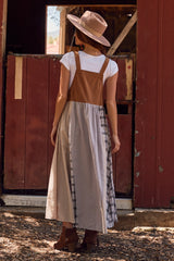 woman wearing a brown and plaid maxi dress with a white t-shirt underneath and a pink wide-brimmed hat