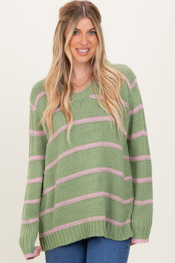 woman wearing a light green striped sweater with pink stripes and a relaxed fit, smiling at the camera