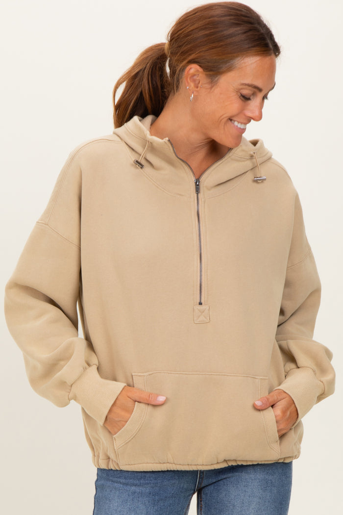 woman wearing a beige oversized hoodie with a half-zip, front pocket, and adjustable drawstring hood