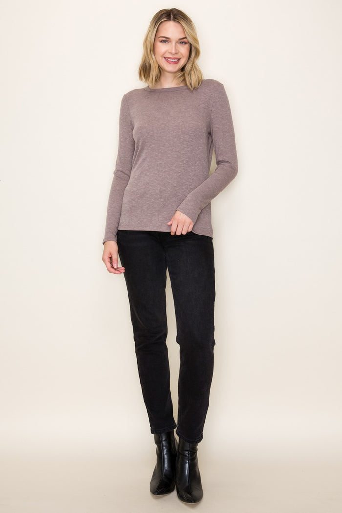 woman wearing a taupe long sleeve sweater and black skinny pants, standing against a light background