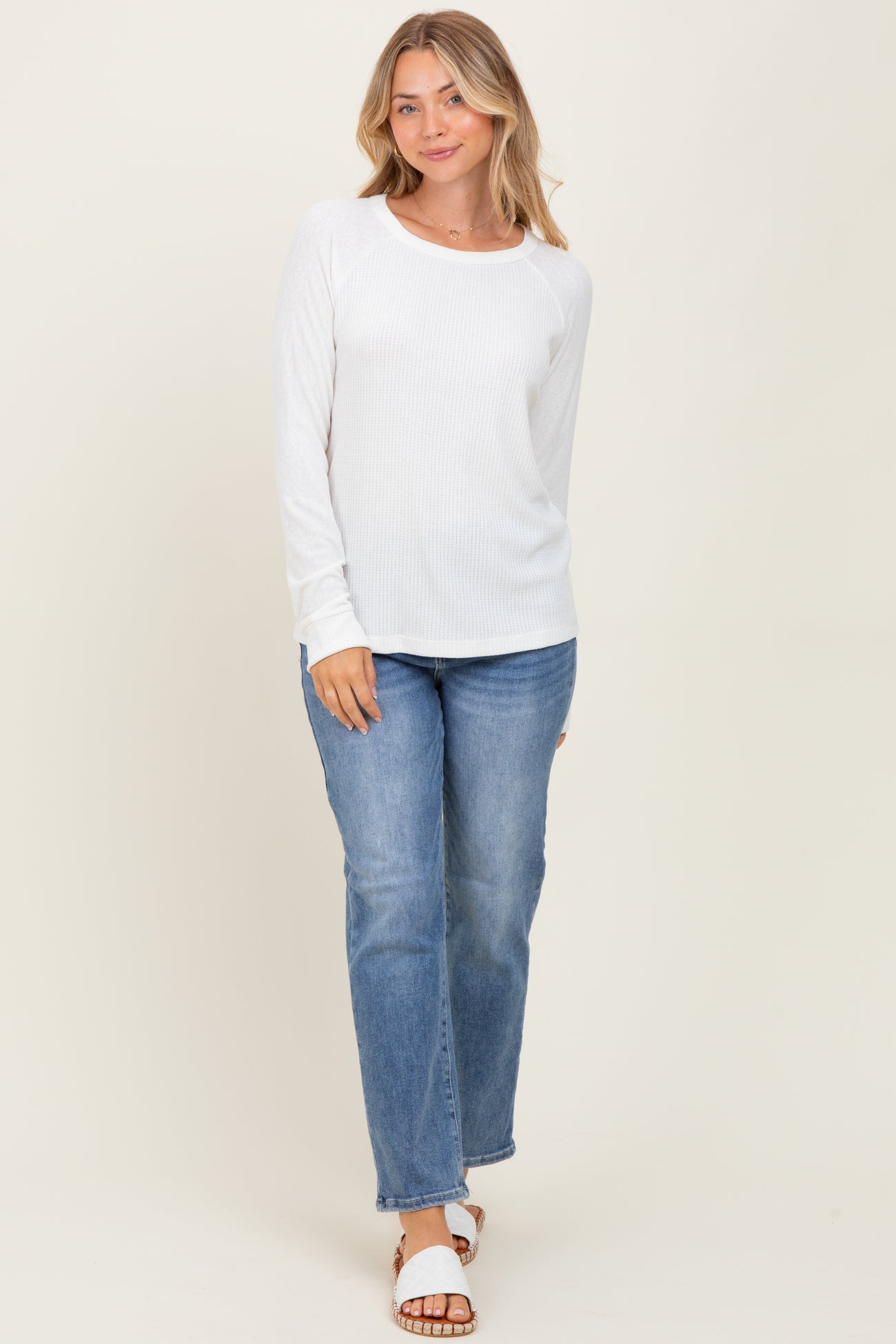 woman wearing a white long sleeve ribbed top with a round neckline and blue straight leg jeans