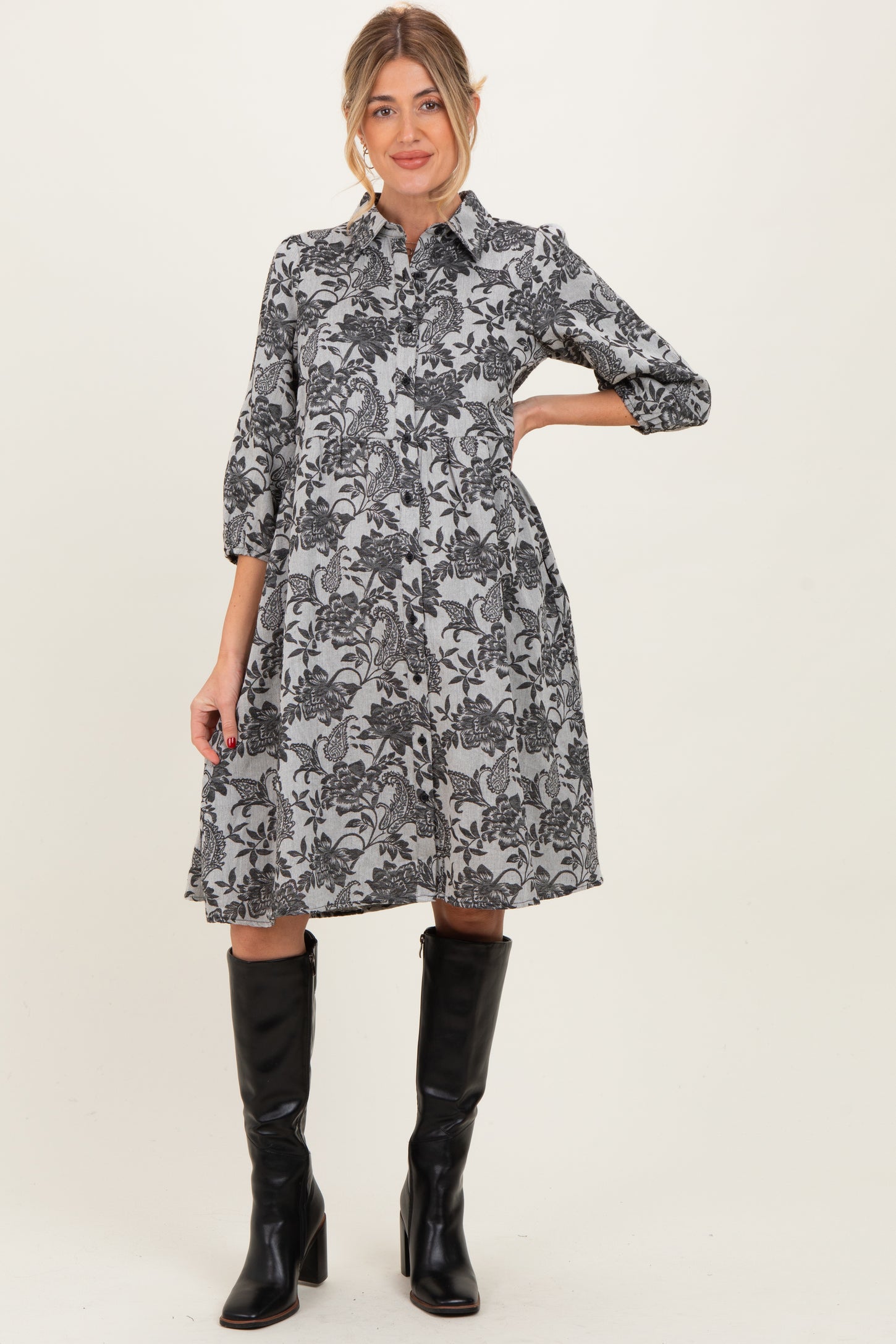 woman wearing a black and white floral maternity dress with three-quarter sleeves and knee-high black boots