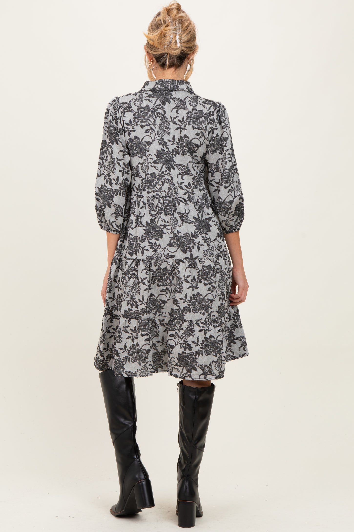 woman wearing a floral patterned maternity dress with three-quarter sleeves and a flowy silhouette, paired with knee-high black boots