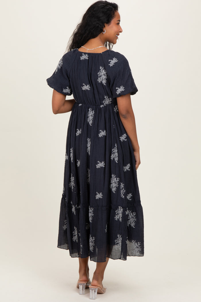 woman wearing a navy blue maternity maxi dress with floral embroidery and tiered design, showing her back