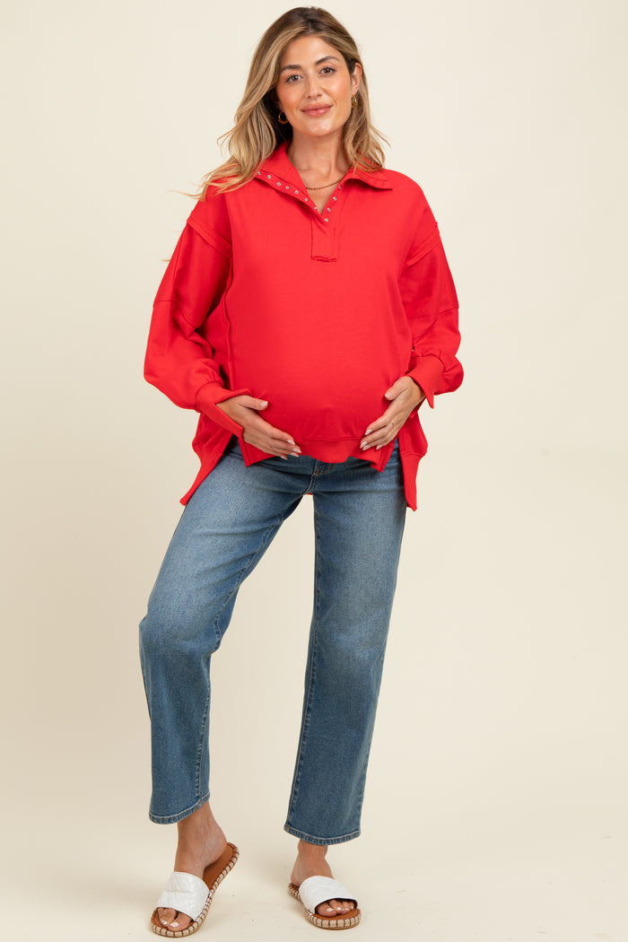 woman wearing a red maternity pullover with a collar and a baby bump, paired with blue jeans and sandals