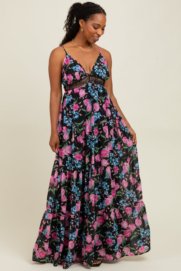 woman wearing a black floral maxi dress with spaghetti straps and a tiered skirt, smiling and standing on a light background