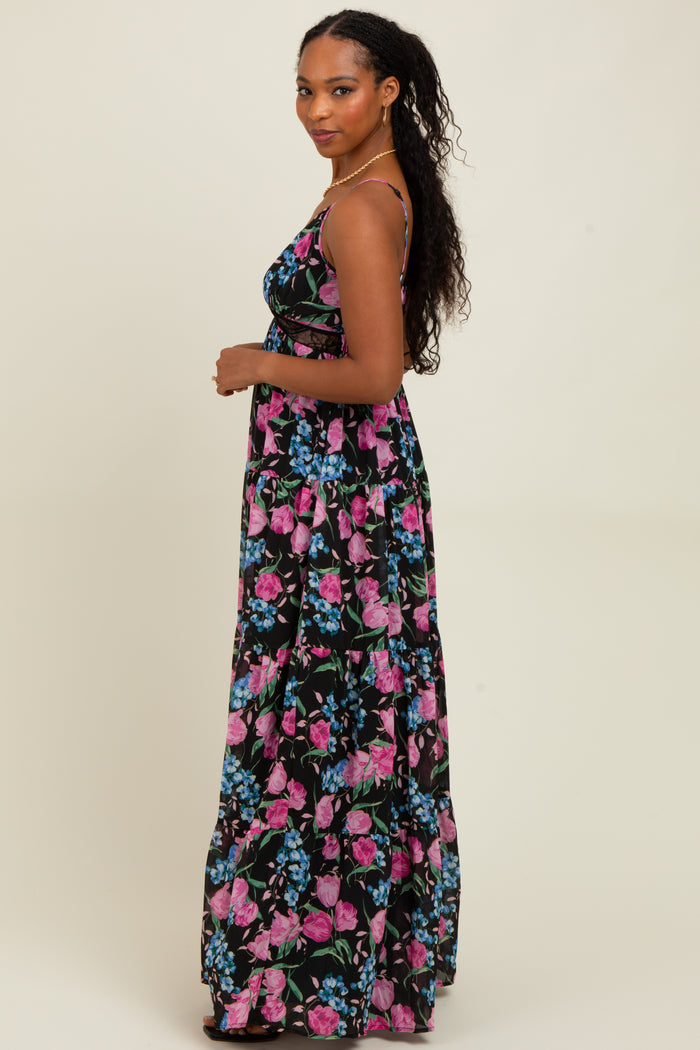woman wearing a black floral maxi dress with pink and blue patterns, posing sideways against a neutral background