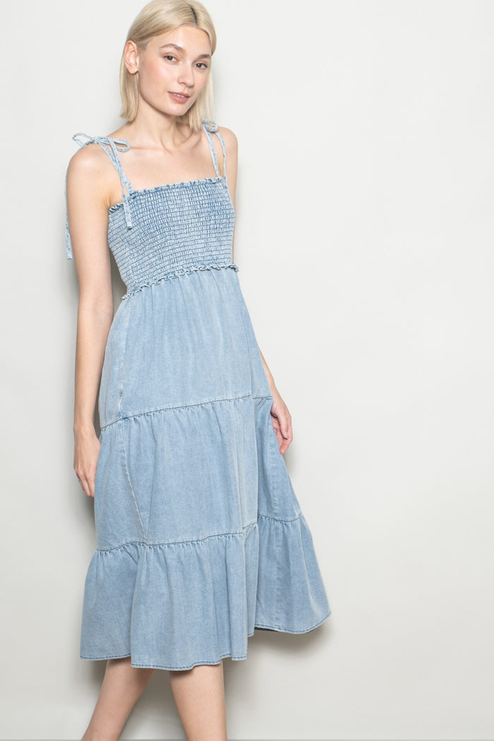 woman wearing a light blue denim tiered midi dress with smocked bodice and spaghetti straps