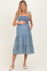 woman wearing a blue denim maternity dress with smocked bodice and tiered skirt, showcasing her baby bump