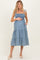 woman wearing a blue denim maternity dress with smocked bodice and tiered skirt, showcasing her baby bump