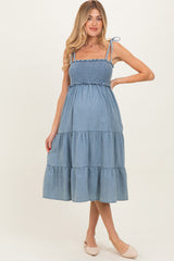 woman wearing a light blue maternity dress with a smocked bodice and tiered skirt, showing a baby bump