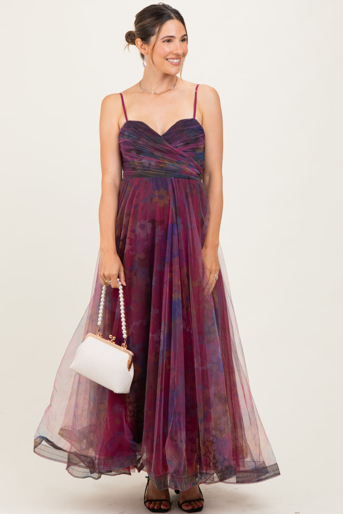 woman wearing a floral multi-color maternity maxi dress with spaghetti straps and holding a white handbag