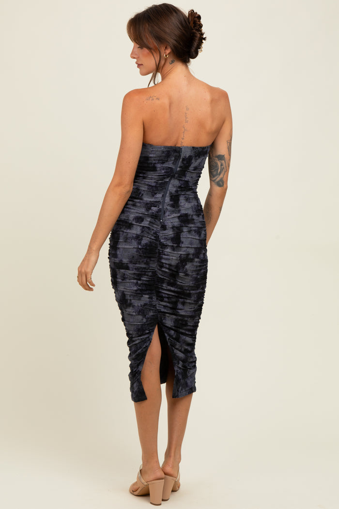 woman wearing a dark blue strapless fitted midi dress with ruching and a back slit, model viewed from the back