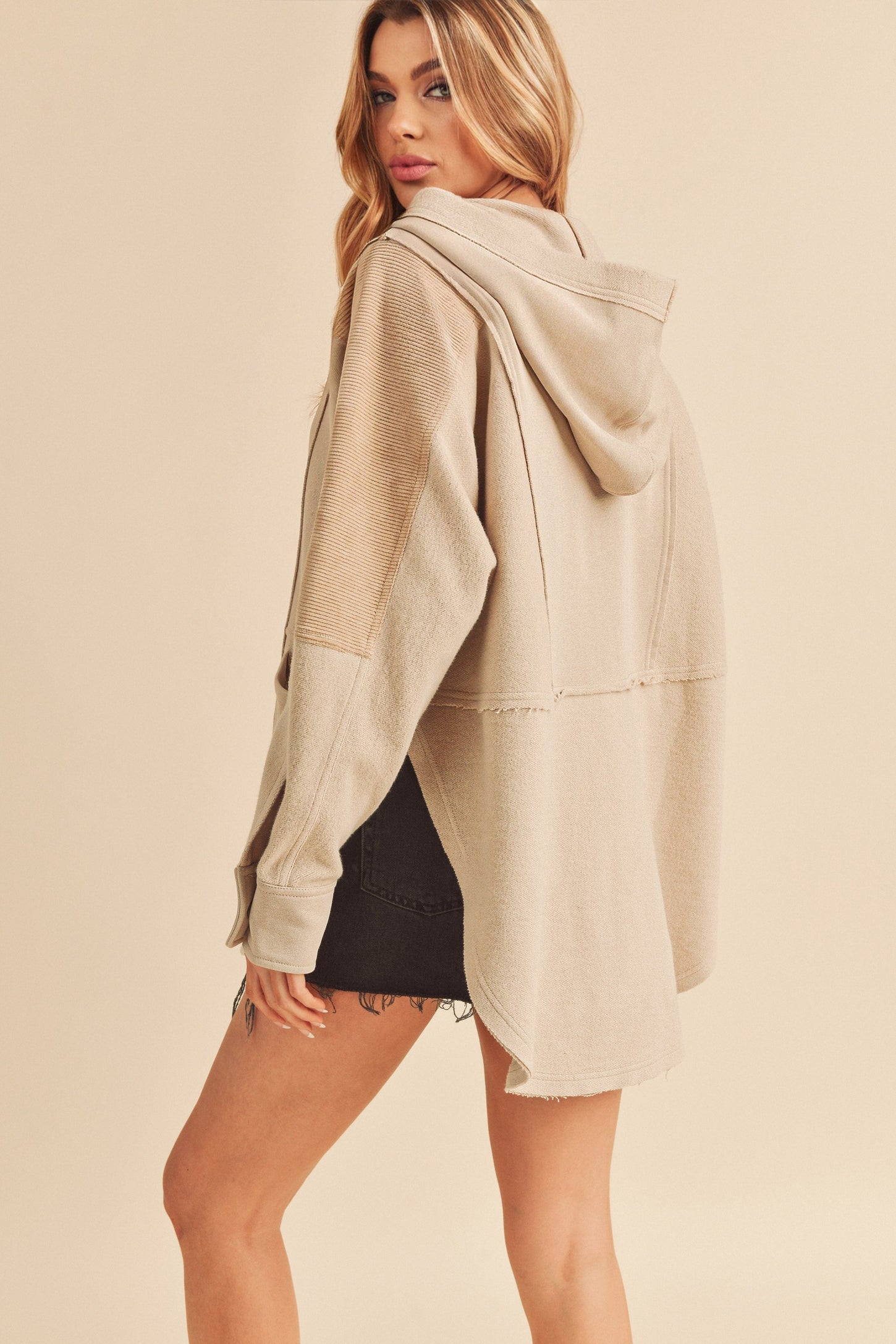 woman wearing a tan oversized hoodie with a hood and frayed hem, styled with a black denim skirt