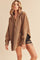 woman wearing a brown oversized hoodie with a front zipper and long sleeves over black distressed shorts