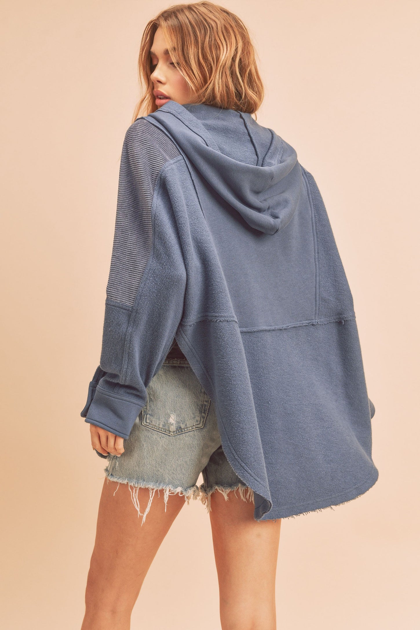 woman wearing a loose-fitting blue hooded sweatshirt with a cropped back and paired with distressed denim shorts