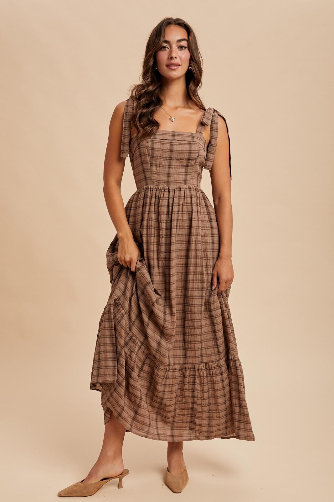 woman wearing a brown plaid midi dress with tie straps and a tiered skirt
