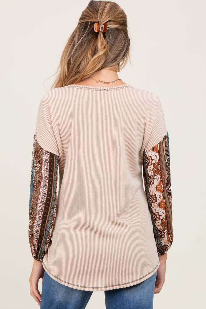 woman wearing a cream ribbed maternity top with patterned balloon sleeves and a curved hem
