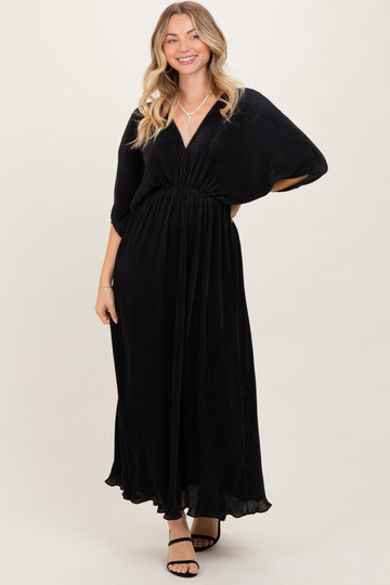 woman wearing a black maxi dress with a deep v-neck and cinched waist, smiling and posing against a light background