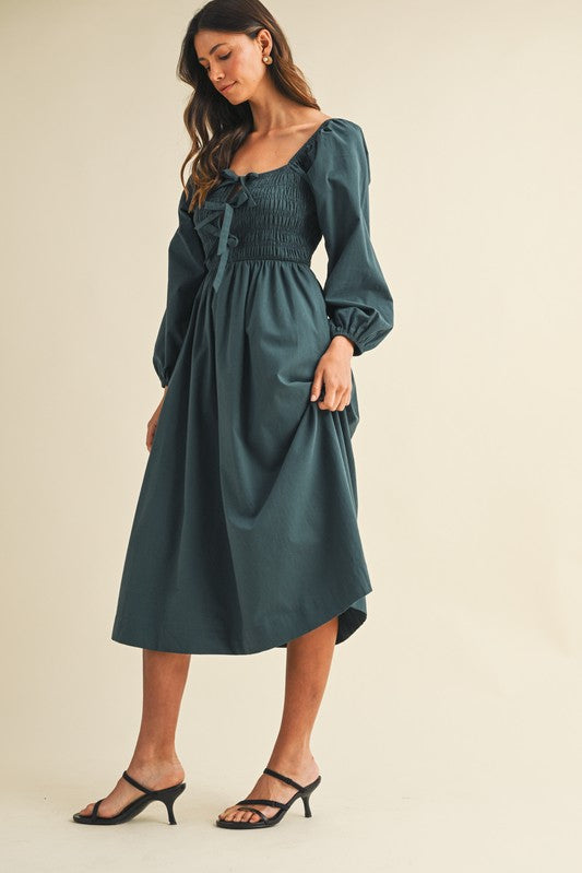 woman wearing a dark teal long sleeve smocked midi dress with puffed sleeves and a gathered bodice
