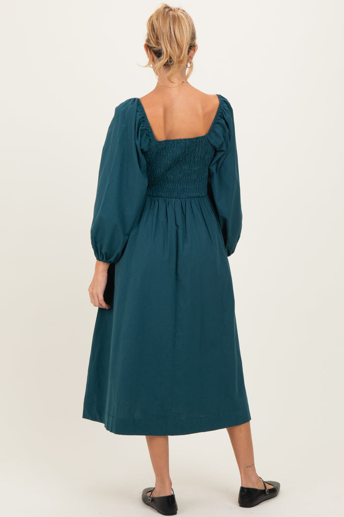 woman wearing a teal maternity midi dress with puff sleeves and a smocked bodice, showing her back