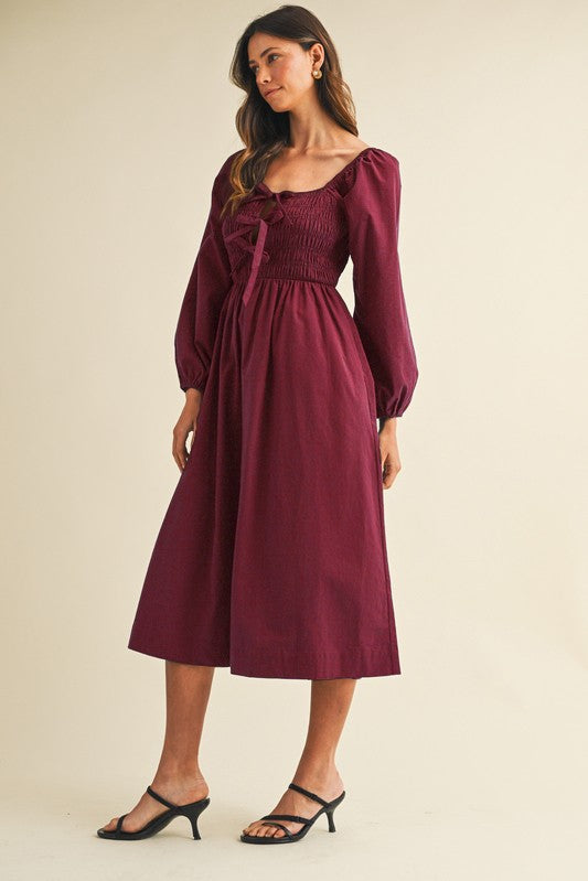 woman wearing a burgundy midi dress with puff sleeves and a smocked bodice, paired with black strappy heels