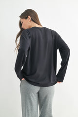 woman wearing a black long sleeve top with a relaxed fit, styled with gray sweatpants, viewed from the back