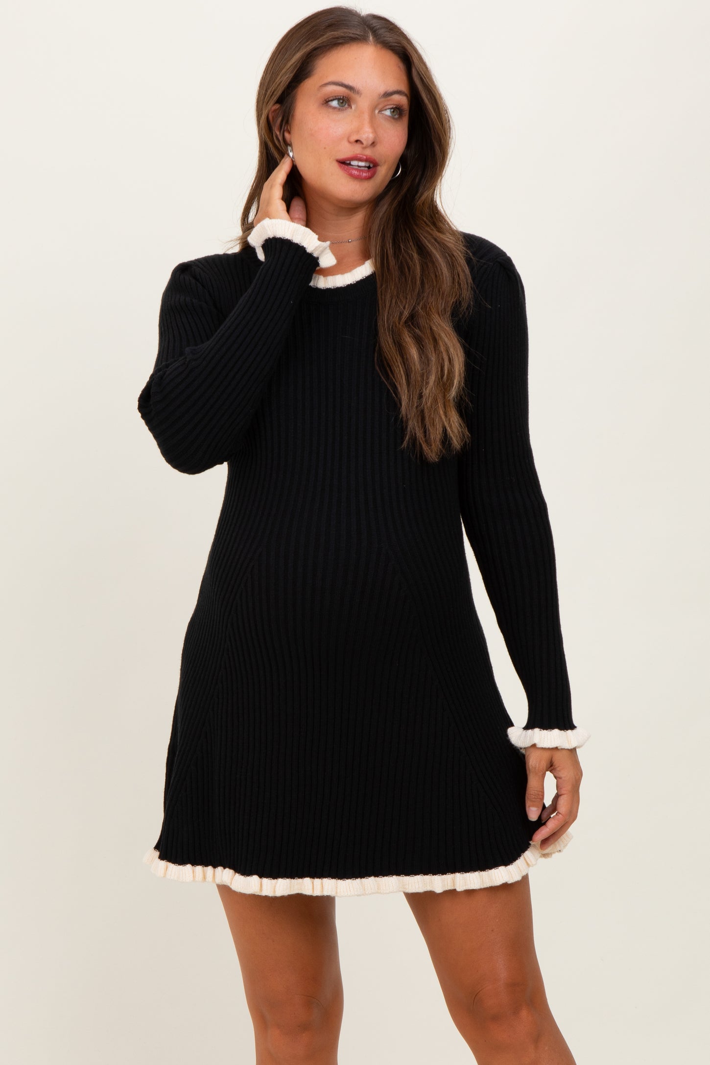 woman wearing a black ribbed maternity dress with cream frill details and long sleeves, showcasing her baby bump