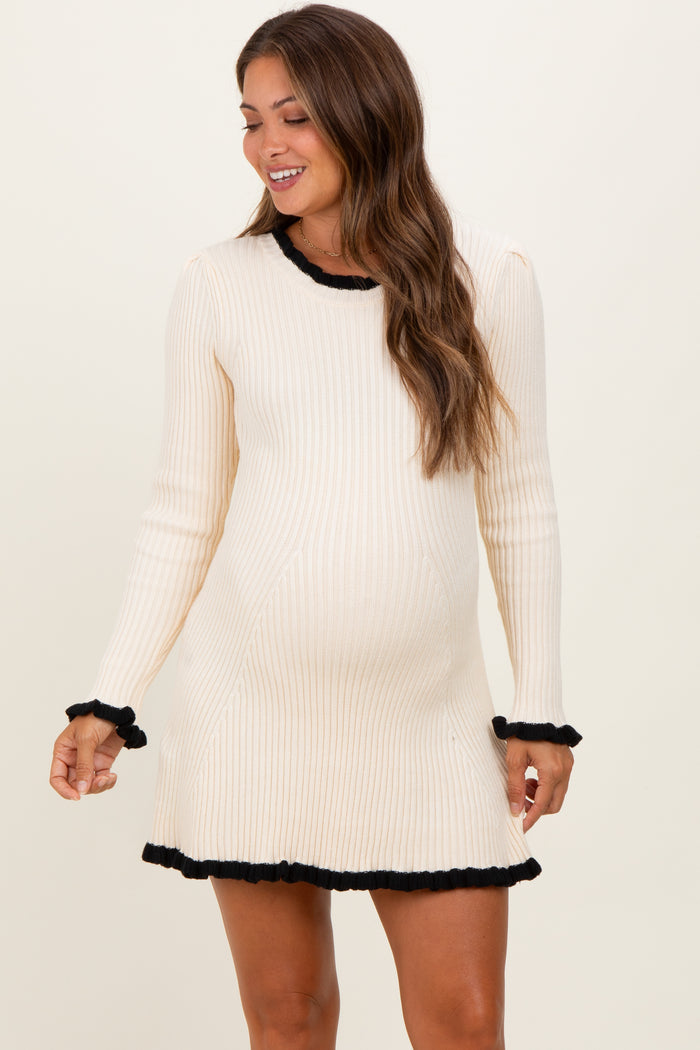 woman wearing a cream ribbed maternity dress with black trim at the neckline and hem, showing her baby bump