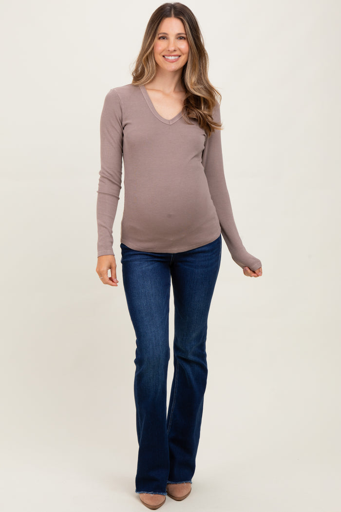 woman wearing a taupe long sleeve v-neck maternity top and flared jeans with a visible baby bump