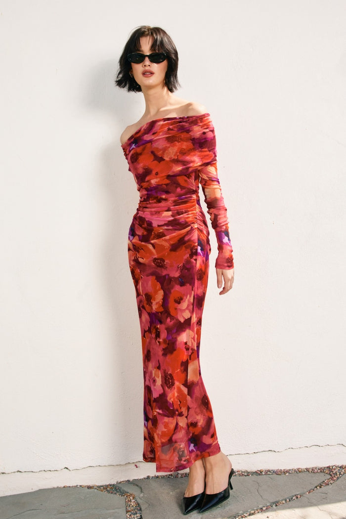 woman wearing a vibrant off-the-shoulder floral maxi dress with long sleeves and black pointy-toed shoes
