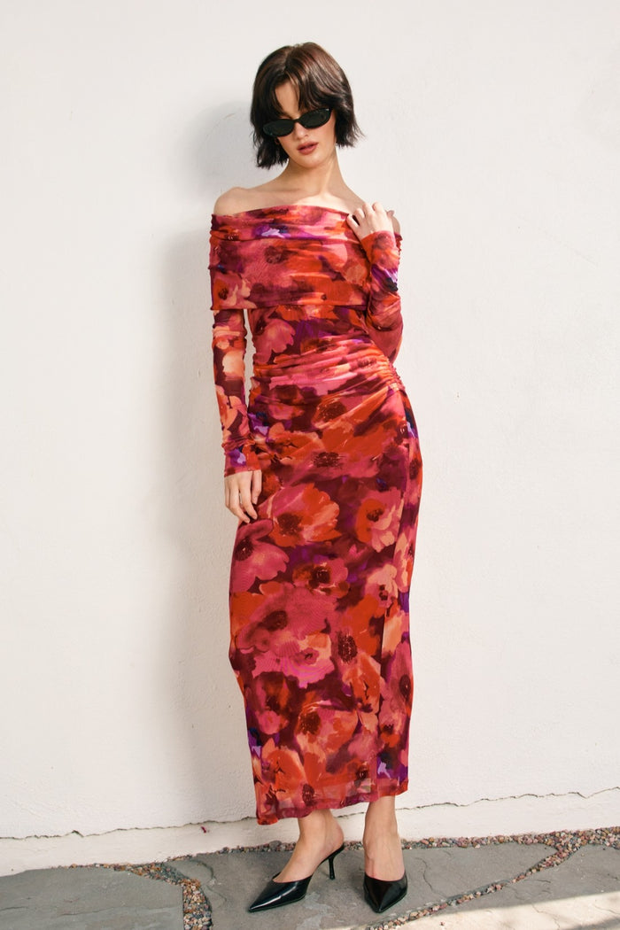 woman wearing a flowy off-shoulder long sleeve floral maxi dress in shades of pink and red, styled with black heels and sunglasses