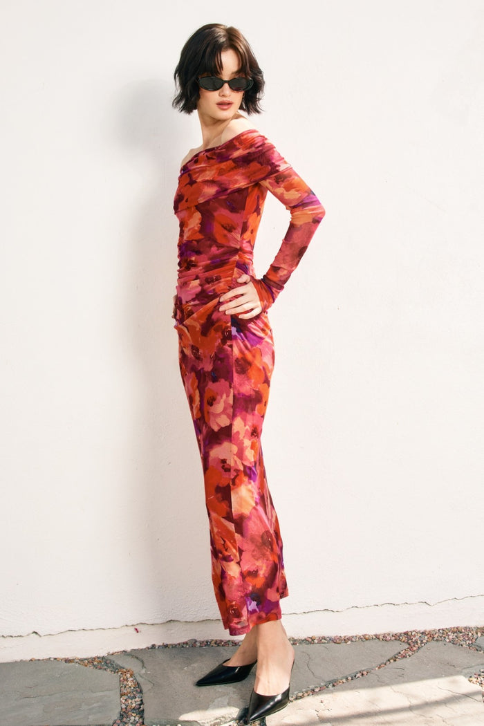 woman wearing a vibrant red and purple floral long sleeve dress with a fitted silhouette and side ruching, accessorized with sunglasses