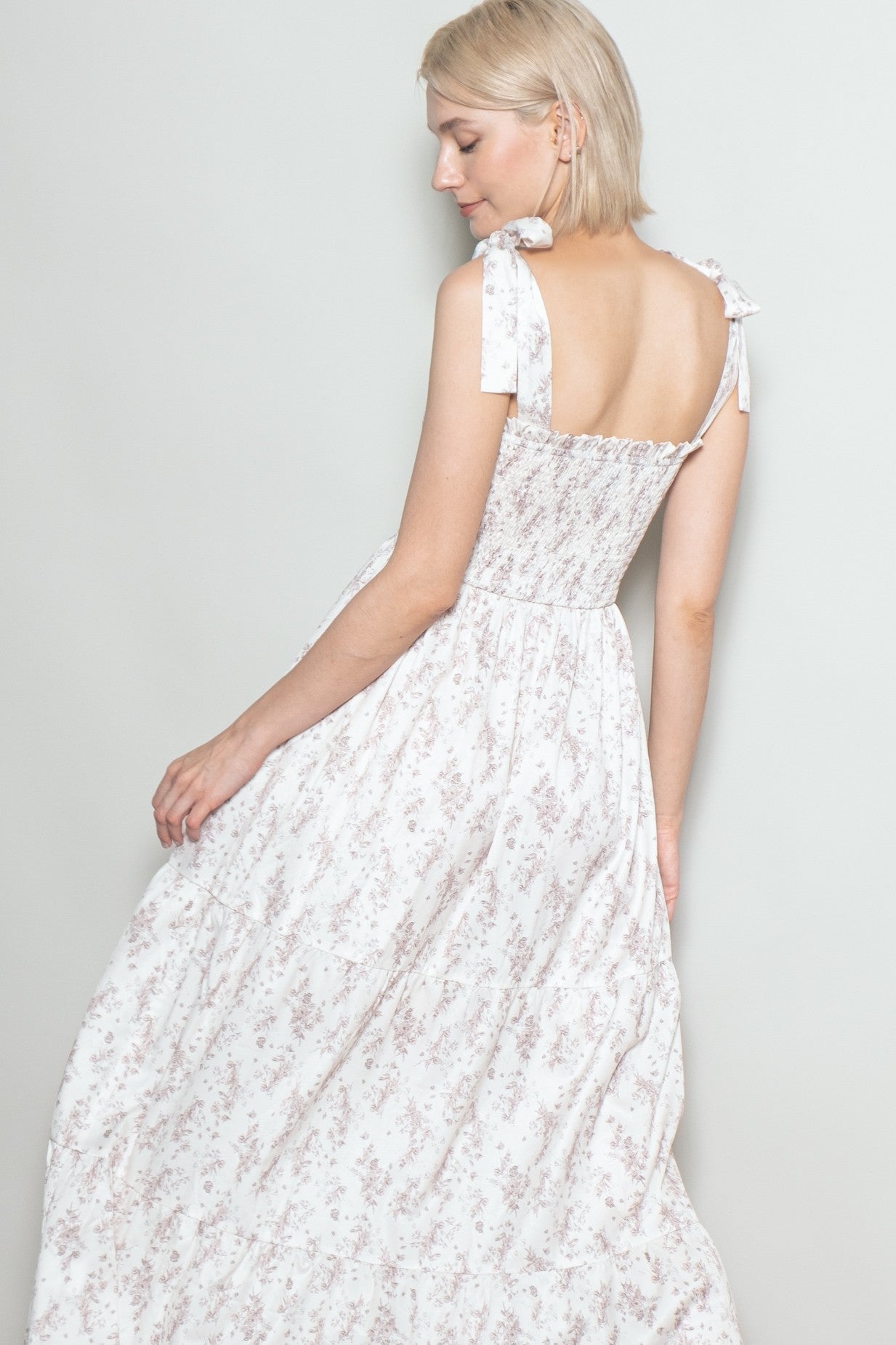 woman wearing a light pink floral maxi dress with tie straps and smocked back detail, photographed from the back