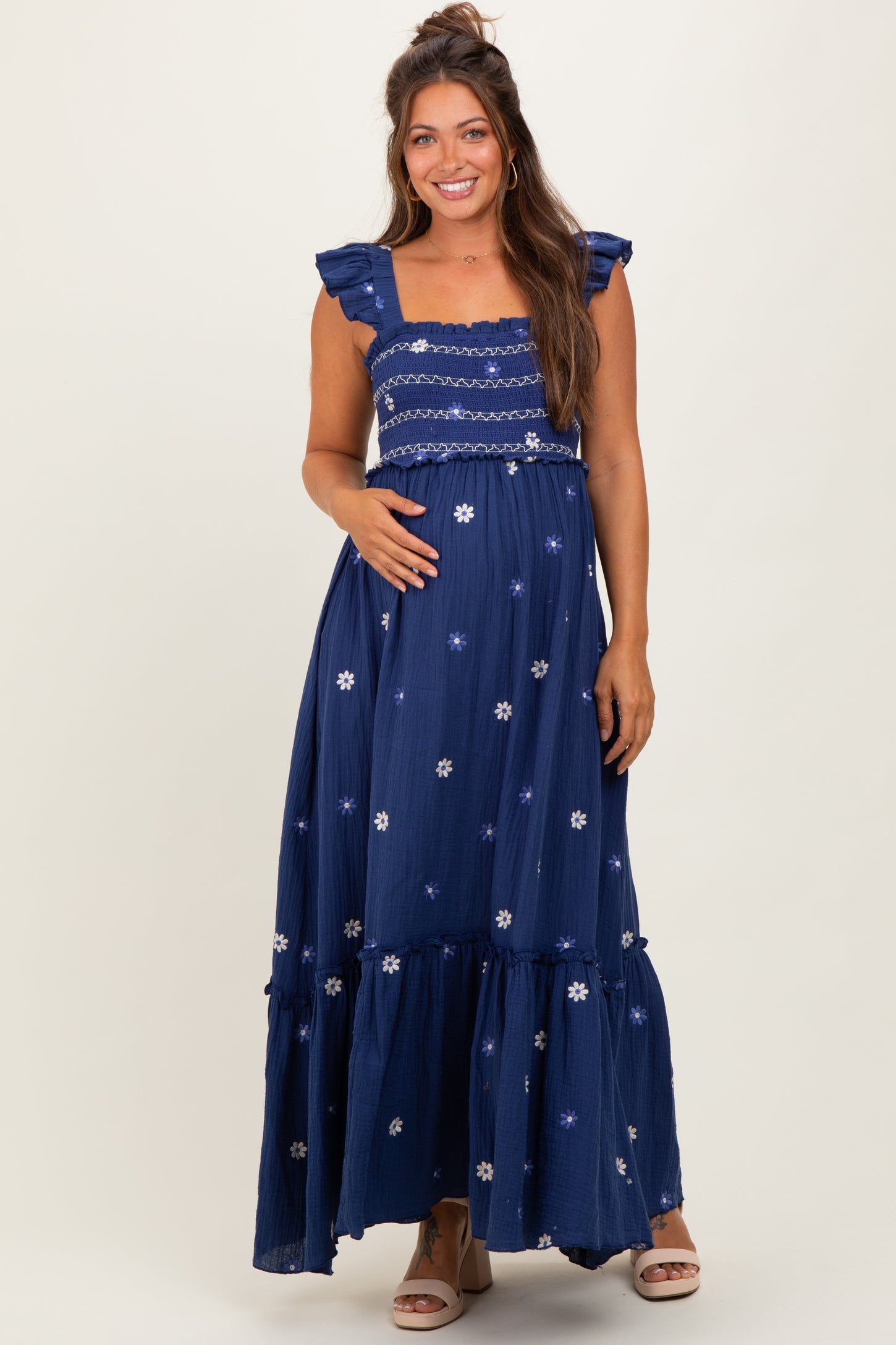 woman wearing a navy blue maternity maxi dress with floral embroidery and ruffled sleeves, showing her baby bump