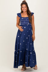 woman wearing a navy blue maternity maxi dress with floral embroidery and ruffled sleeves, showing her baby bump