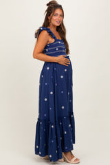 woman wearing a navy blue floral embroidered maternity maxi dress and cradling her baby bump